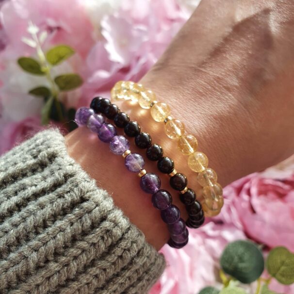 Three crystal bracelets on wrist – black obsidian, clear quartz, and amethyst stacked for protection, clarity, and spiritual balance.